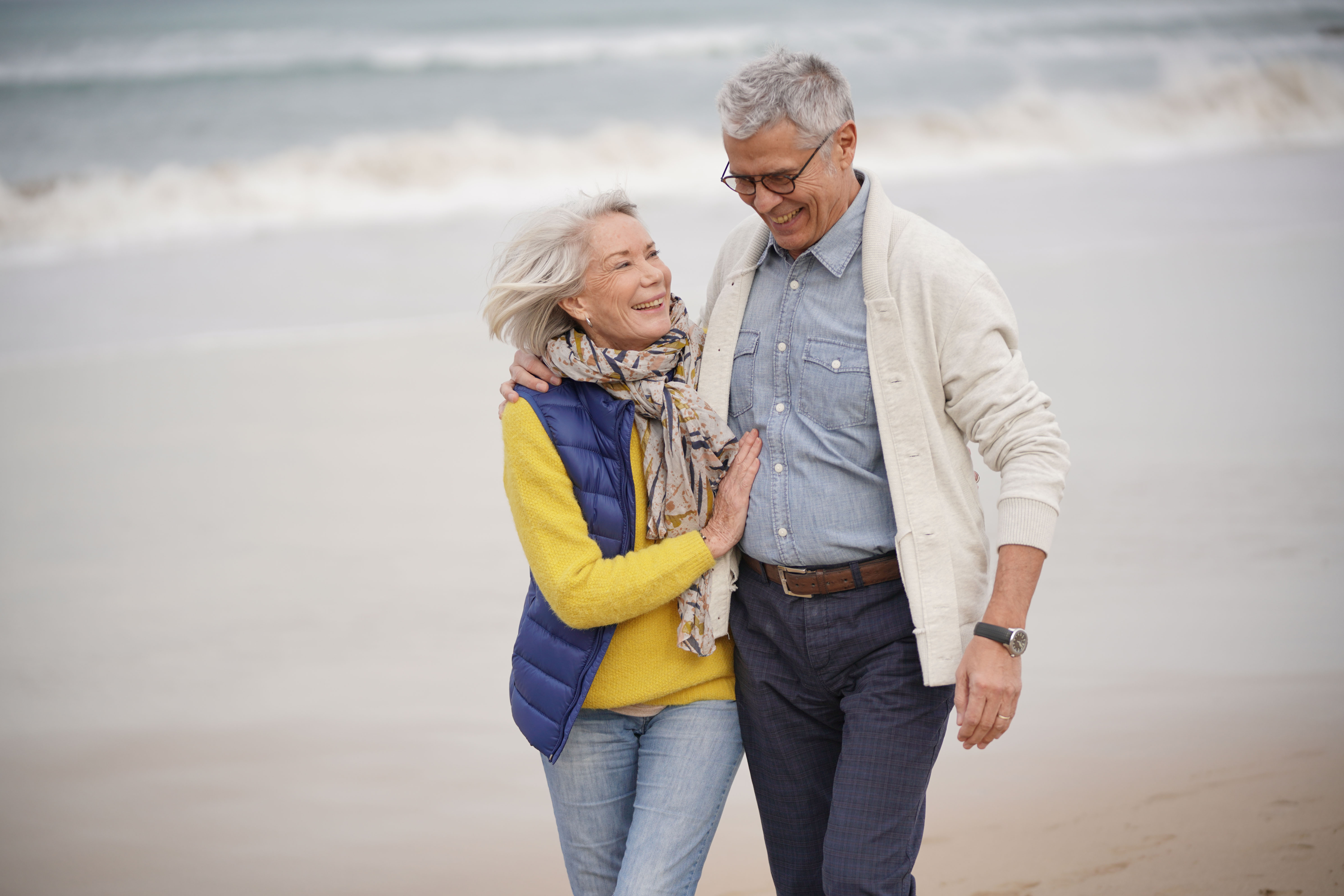 Man and woman walking arm in arm on a windy beach