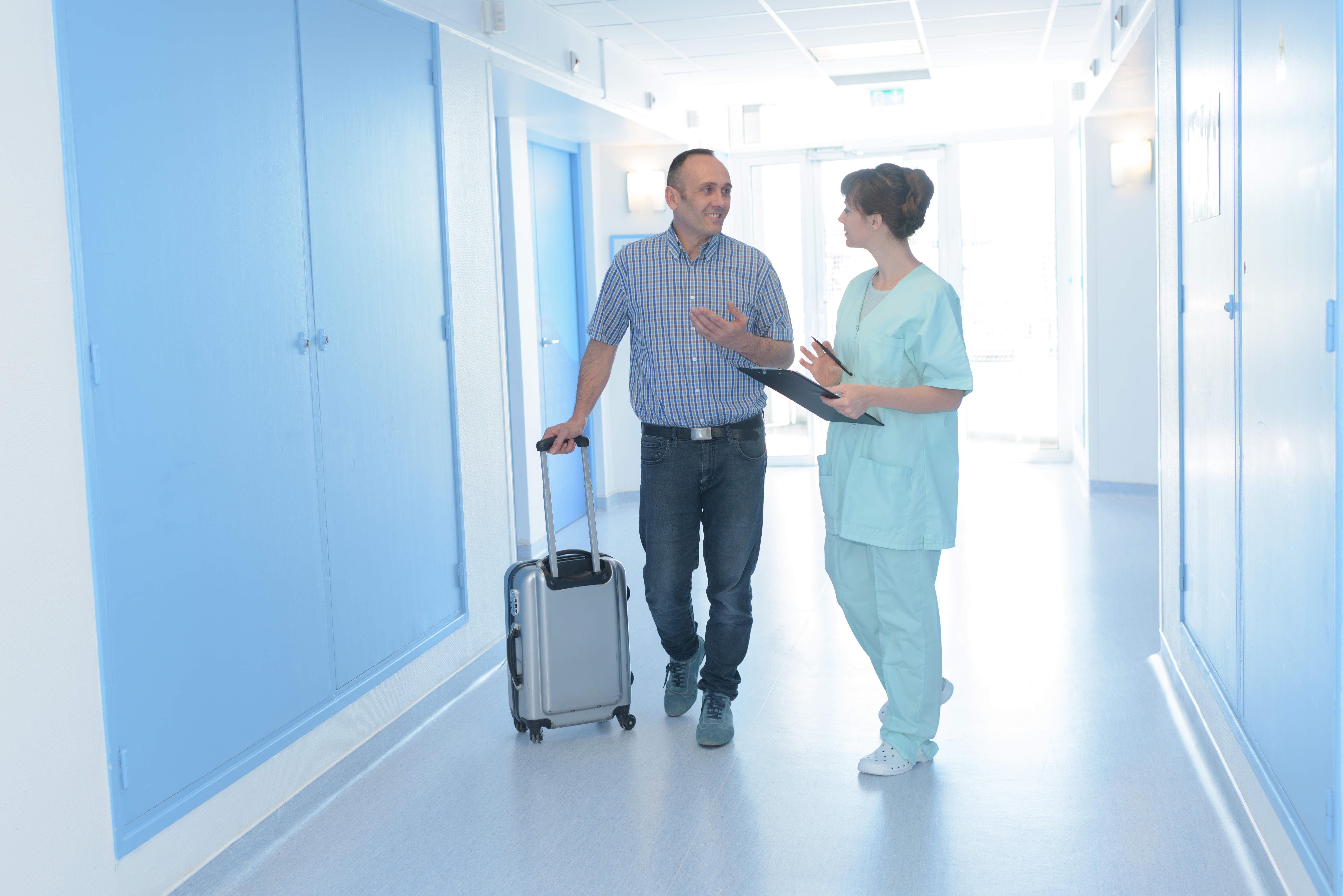 Man with suitcase in hospital corridor talking to nurse