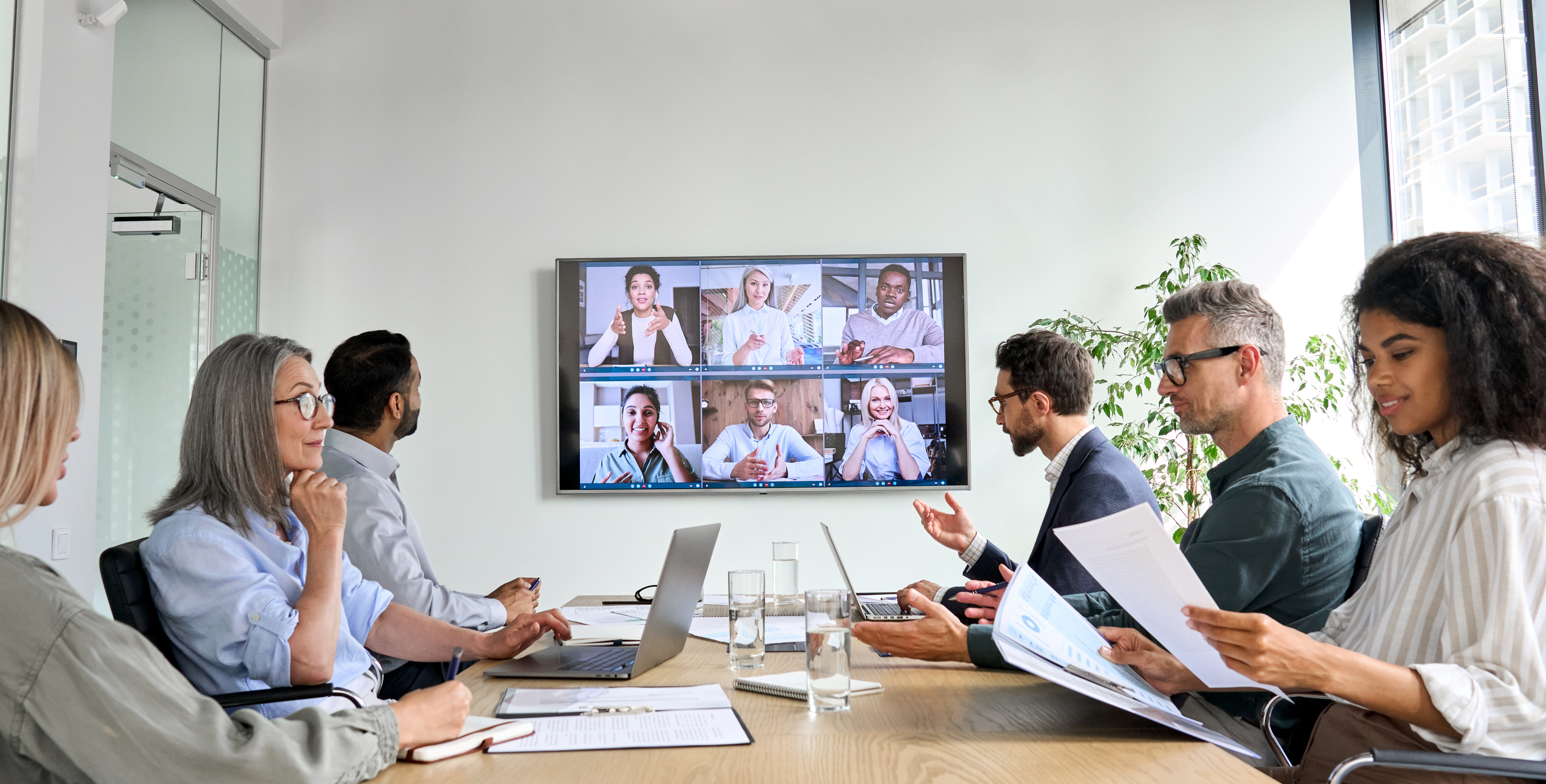 People sitting around a large table looking a Zoom screen