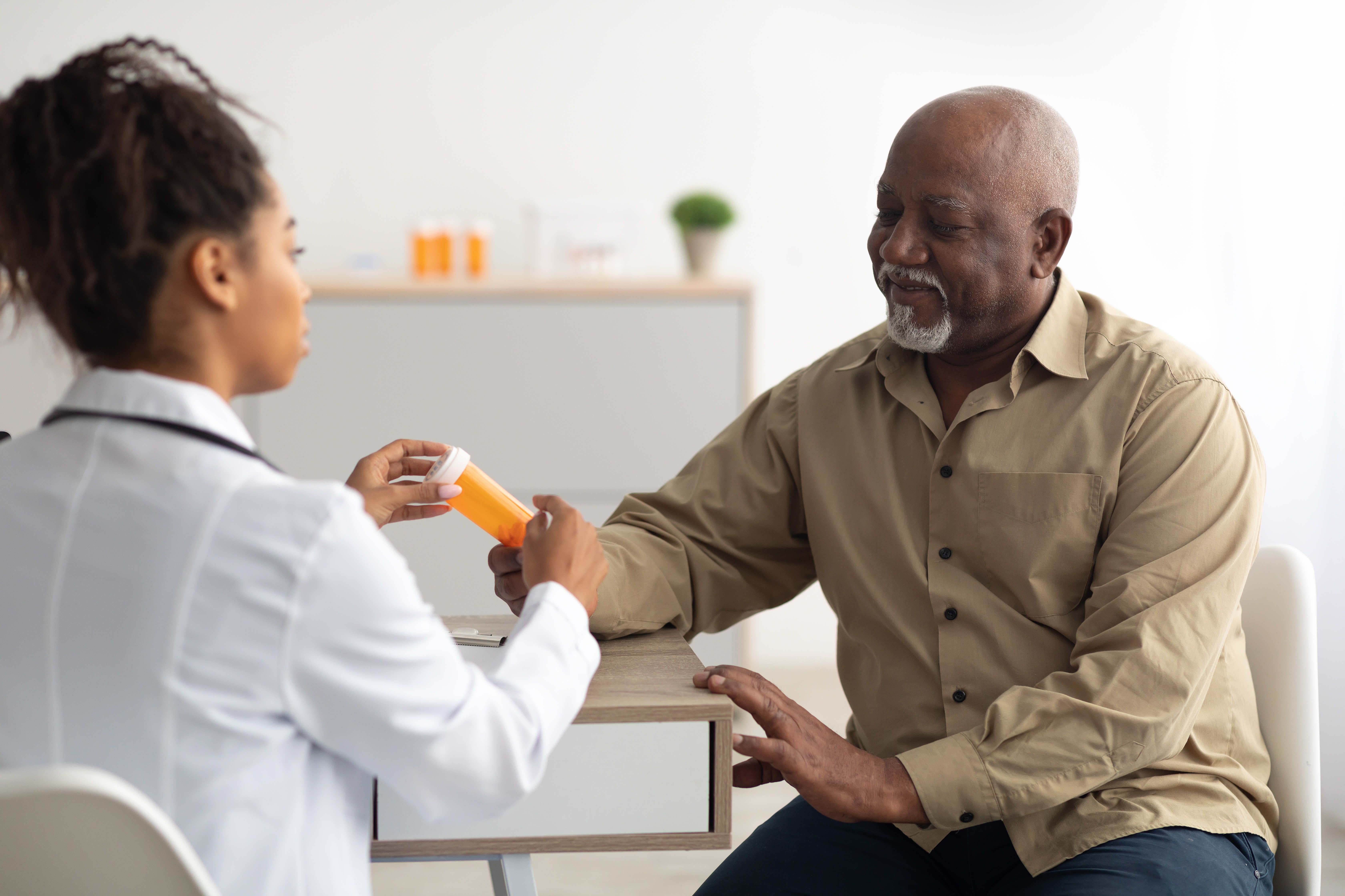 Black man handing pee sample bottle to nurse