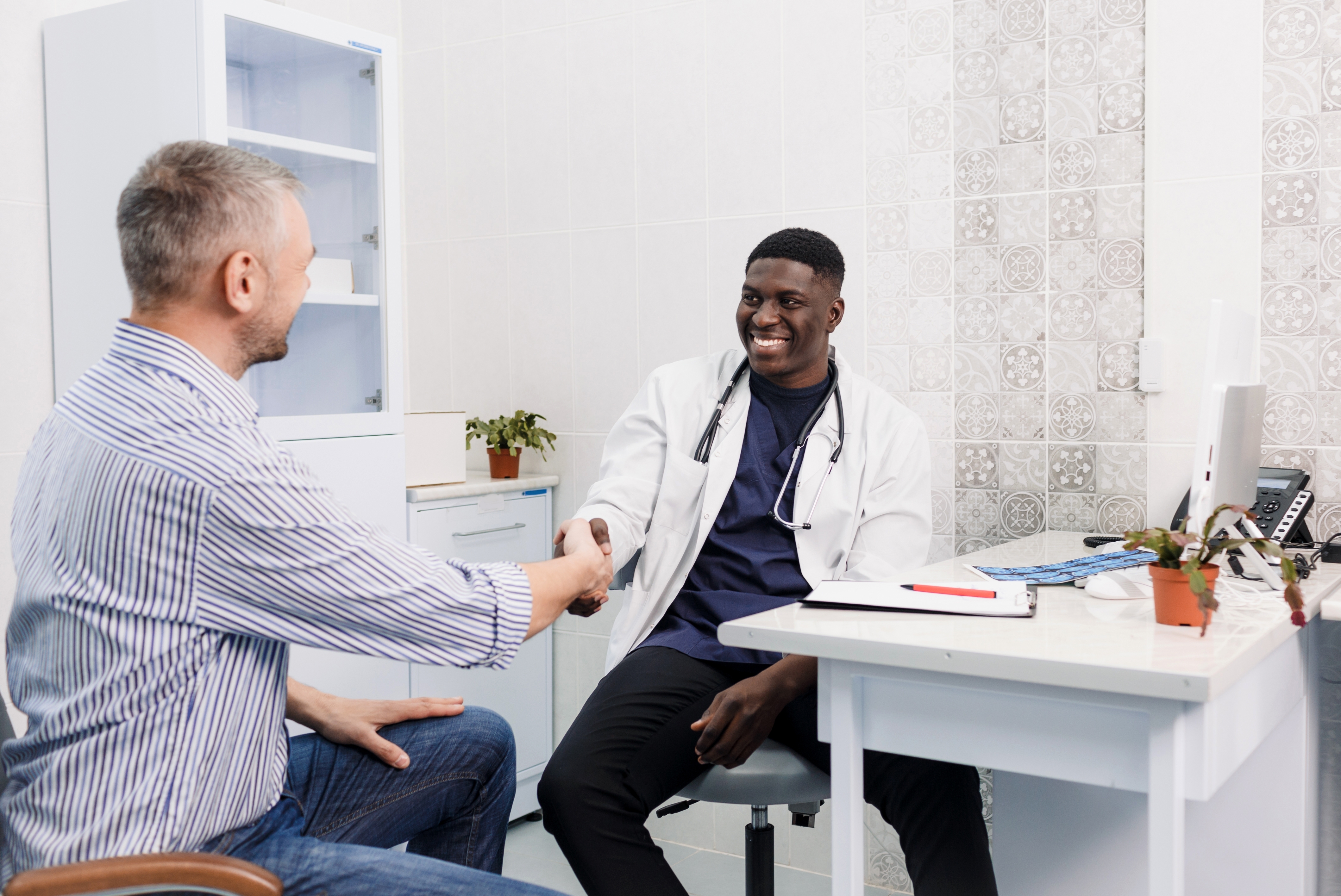 Black doctor smiling shaking hands with White middle aged male patient